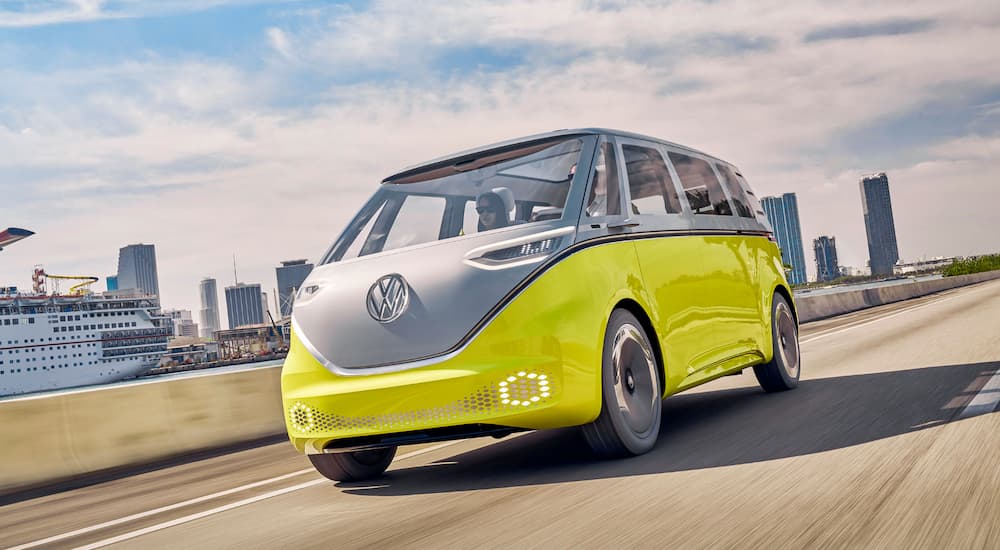 A yellow and white prototype VW ID. BUZZ is driving away from a city.