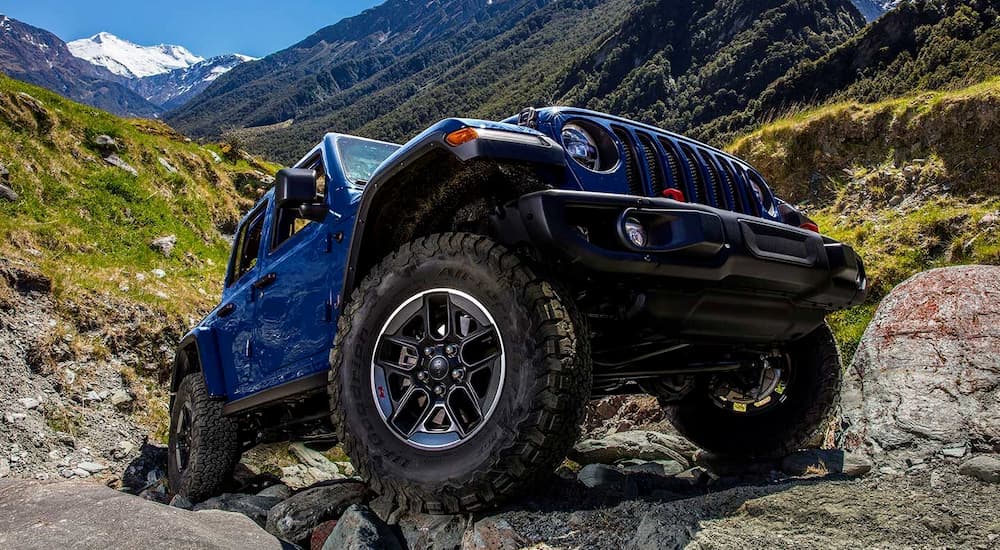 A blue 2019 Jeep Wrangler is off-roading near mountains.