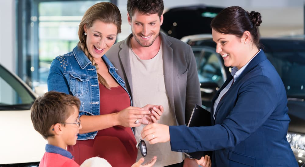 A saleswoman is handing a family the keys to their new car at a dealership they found by searching 'used car dealership near me'.