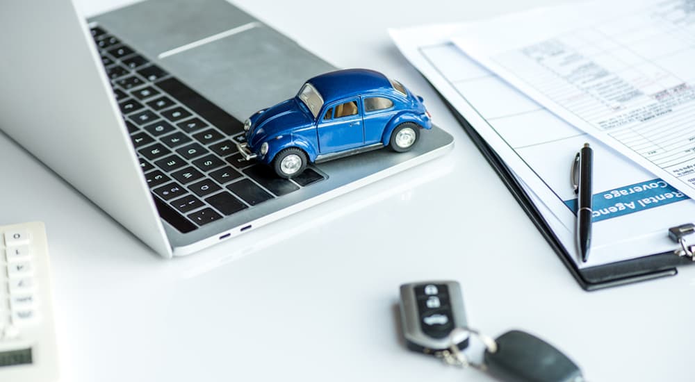 A blue toy car is on a laptop next to car keys.