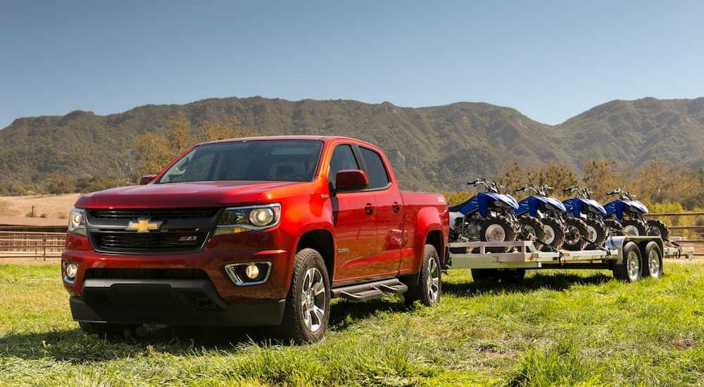 A red 2019 Chevy Colorado is in a field towing a trailer full of atvs. 
