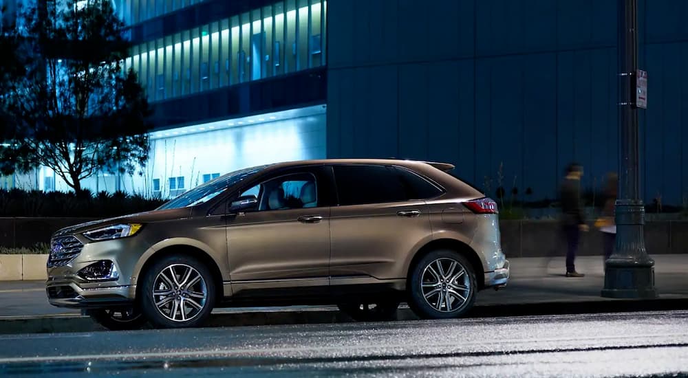 A tan 2019 Ford Edge, which wins when comparing the 2019 Ford Edge vs 2019 Hyundai Santa Fe, is parked in the city at night.