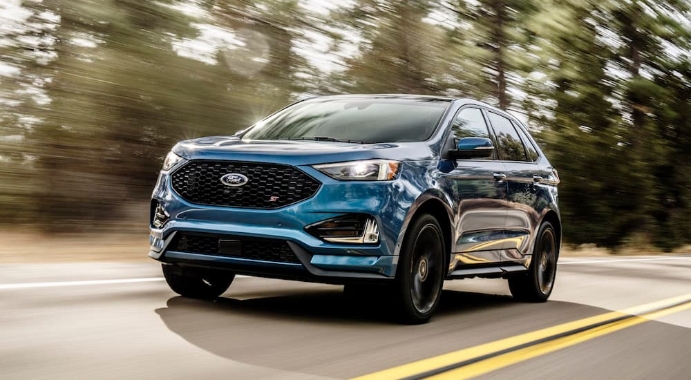 A blue 2019 Ford Edge, which wins when comparing the 2019 Ford Edge vs 2019 Nissan Murano, is driving past trees quickly.