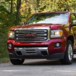 A red 2019 GMC Canyon is driving on a tree-lined road.
