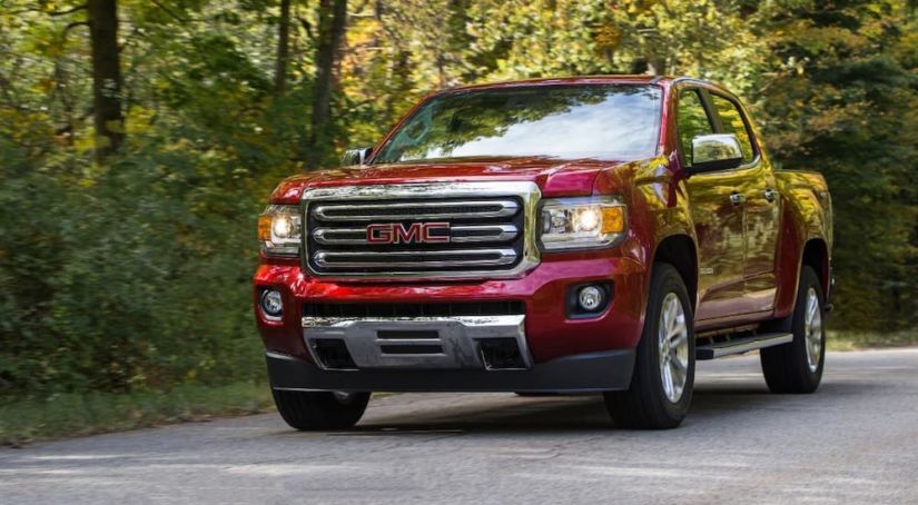 A red 2019 GMC Canyon is driving on a tree-lined road.