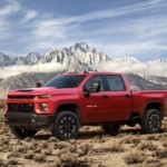 A red 2020 Chevy Silverado 2500HD is in front of snowy mountains.