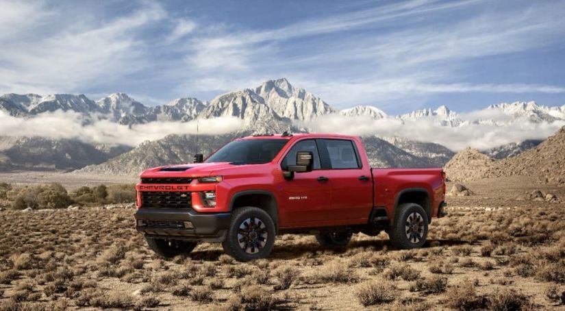 A red 2020 Chevy Silverado 2500HD is in front of snowy mountains.