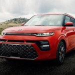 A red 2020 Kia Soul is parked with a hill in the distance.