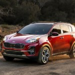 A red 2020 Kia Sportage is parked on a dirt path with dust flying in the air.