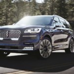 A blue 2020 Lincoln Aviator is driving around a corner uphill.