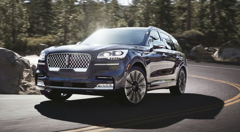 A blue 2020 Lincoln Aviator is driving around a corner uphill.