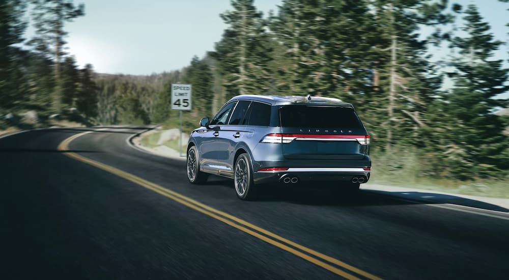 A blue 2020 Lincoln Aviator is driving past pine trees.