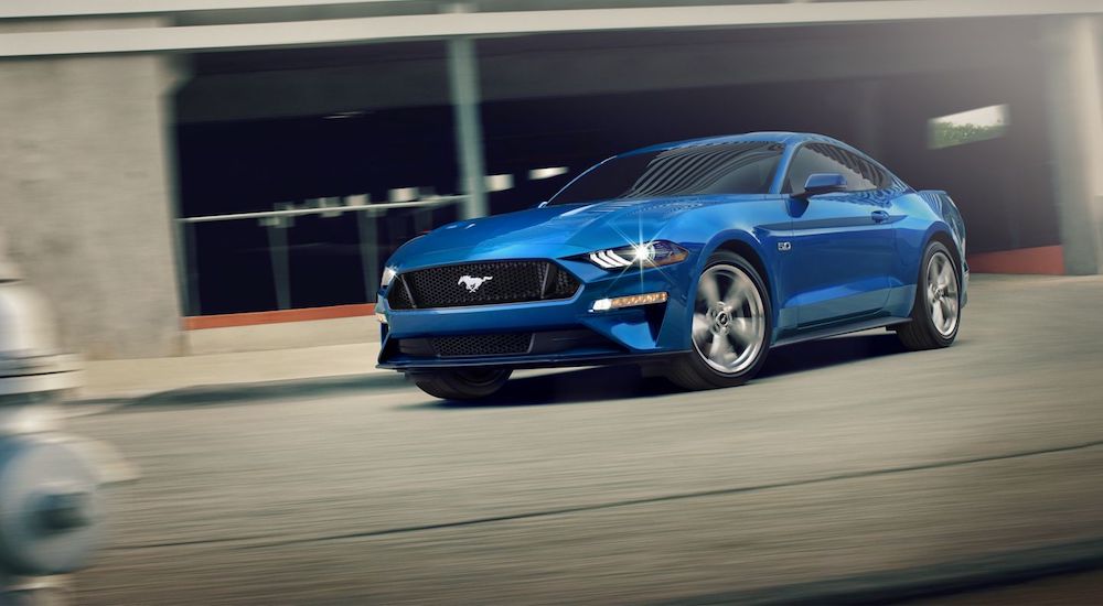A blue 2020 Ford Mustang is driving on a city street on a sunny day. 