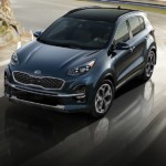 A blue 2020 Kia Sportage is driving around a corner with a sunset in the background,