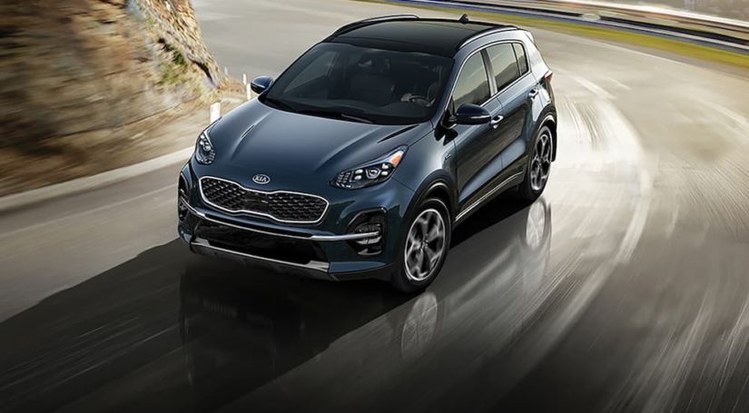 A blue 2020 Kia Sportage is driving around a corner with a sunset in the background,