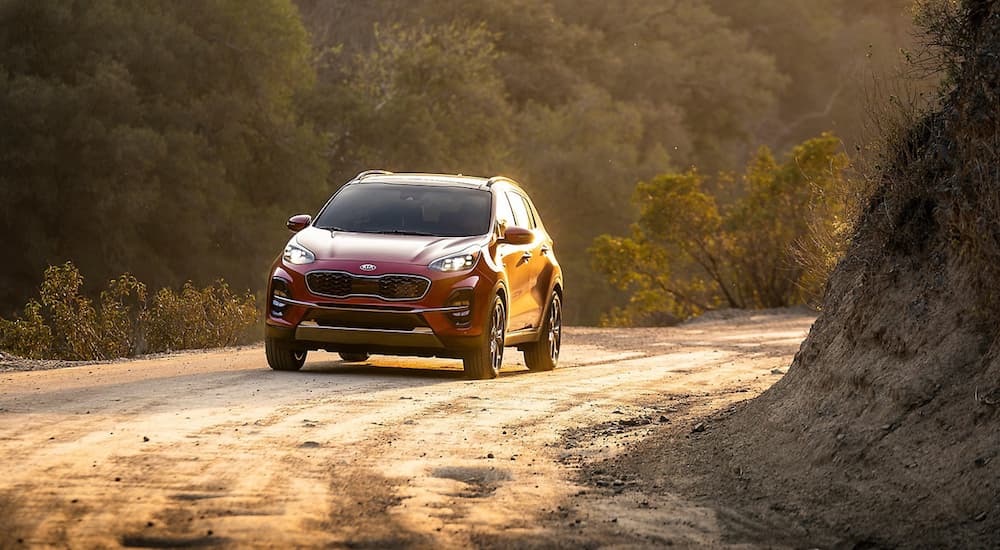 The 2020 Sportage is shown driving on a dirt road with the sun in the background.