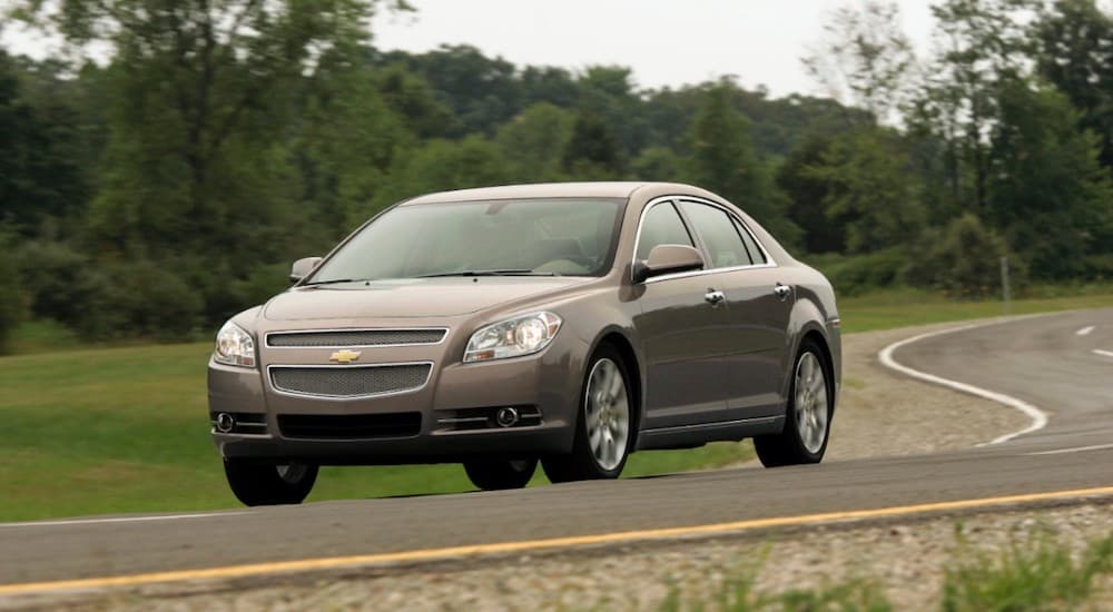 A tan 2012 Chevy Malibu, an option for used cars under 10k, is on a winding road.