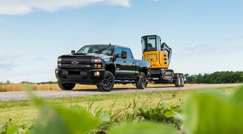 A black 2018 Chevy Silverado 2500HD is shown towing work equipment with fields in the background. 
