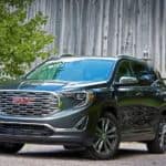 A grey GMC terrain, which wins when comparing the 2019 GMC Terrain vs 2019 Toyota RAV4, is parked in front of a grey wooden barn.