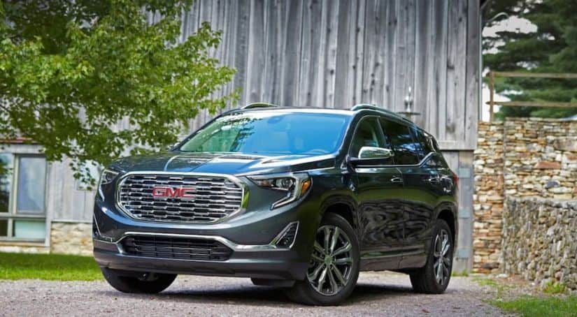 A grey GMC terrain, which wins when comparing the 2019 GMC Terrain vs 2019 Toyota RAV4, is parked in front of a grey wooden barn.