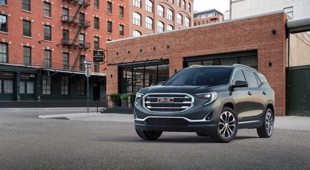 A grey 2019 GMC Terrain is parked in front of brick buildings on a city street. 