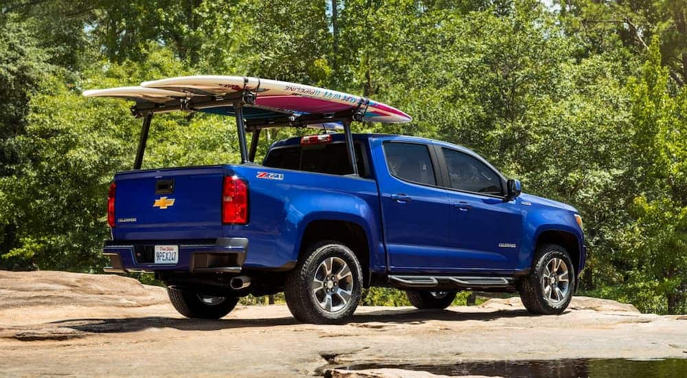 A blue 2019 Chevy Colorado is parked on dirt with paddle boards on the bed rails.