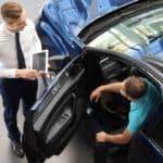 A sales person is talking to a buyer sitting in a blue car.