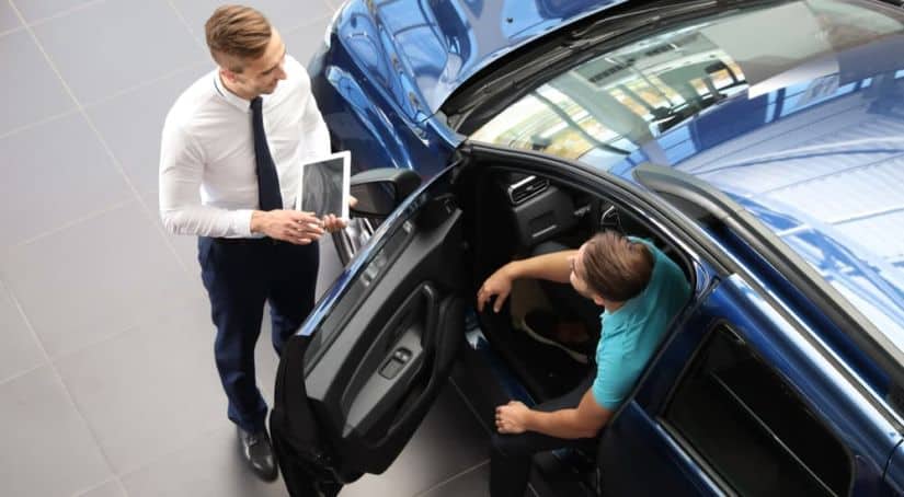 A sales person is talking to a buyer sitting in a blue car.