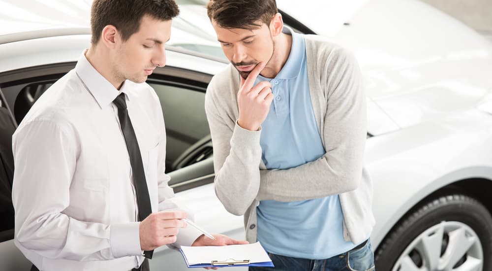 A car salesman at a no credit car lot is showing a clipboard to a buyer.