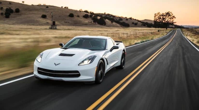 A white 2016 Chevy Corvette is driving on a straight road at sundown.