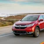 A red 2018 Honda CR-V, popular among used cars for sale, is driving on an ocean road.