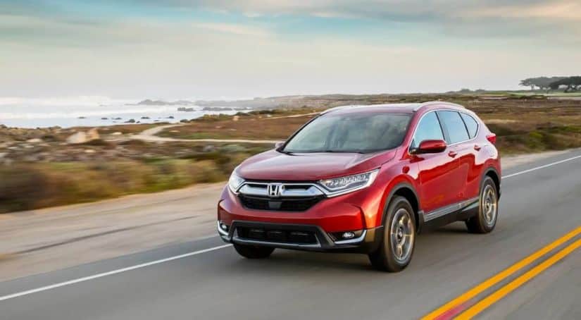 A red 2018 Honda CR-V, popular among used cars for sale, is driving on an ocean road.
