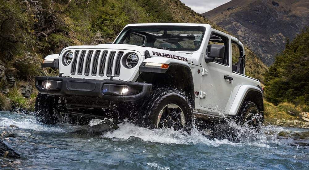 A white 2018 used Jeep Wrangler for sale is off-roading in a river.