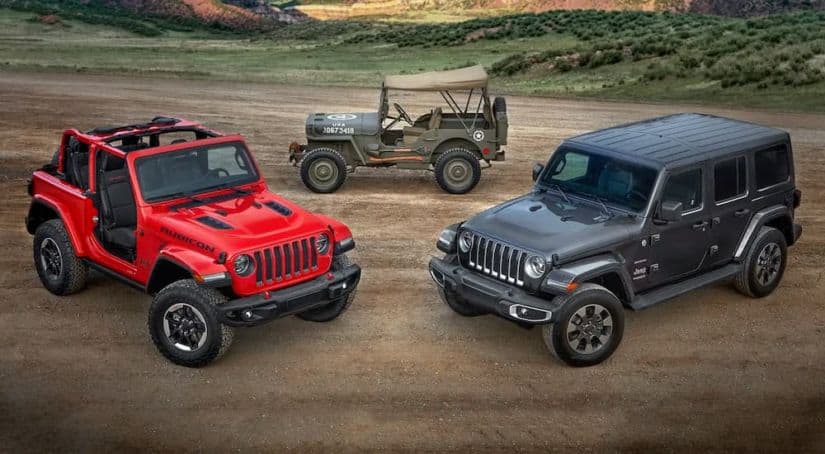 Two 2018 Jeep Wranglers are in front of an antique military Jeep.