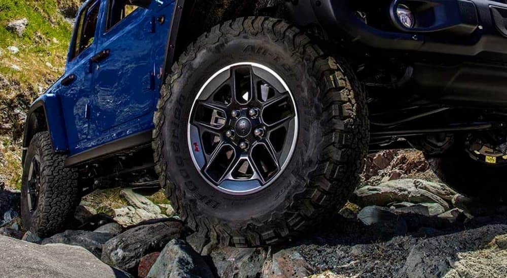 The wheel of a blue 2019 Jeep Wrangler is shown on a rock.
