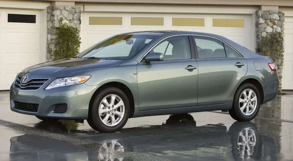 A light green 2011 Toyota Camry, popular among used cars, is parked in front of garage doors.