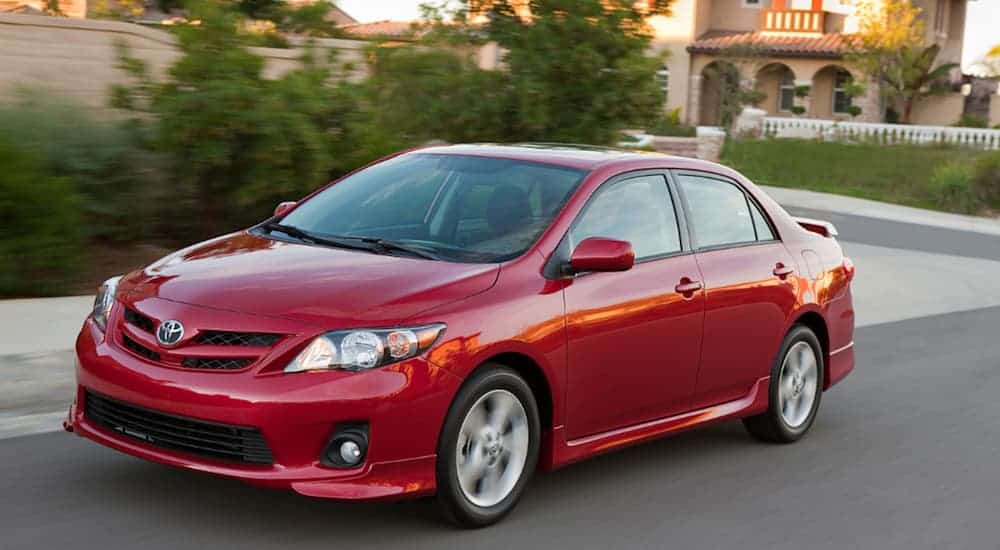 A red 2011 Toyota Corolla is driving on a treelined road.