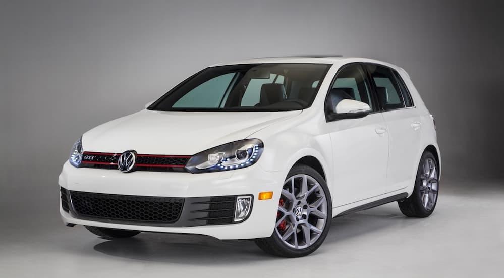 A white 2014 Volkswagen GTI is parked in a grey display room.