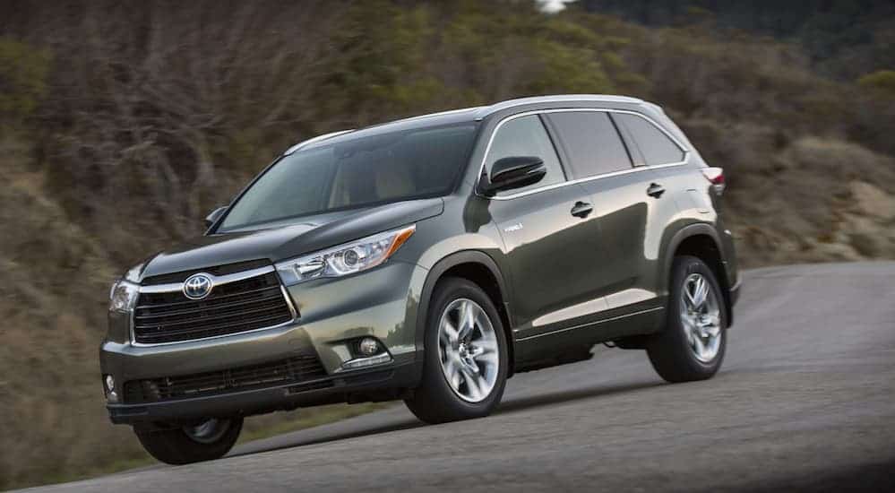 A grey 2016 Toyota Highlander, popular among most used cars, is driving on a treelined highway. 