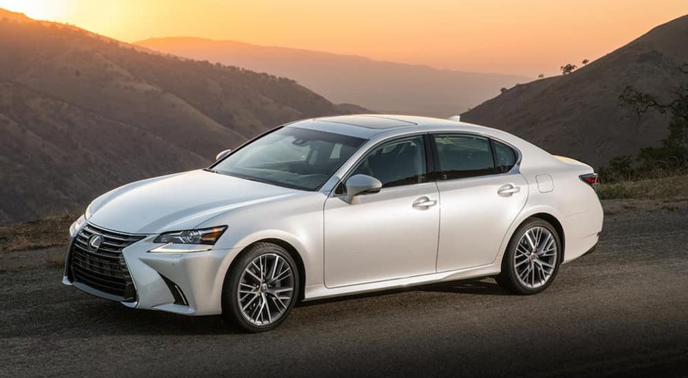 A white 2017 Lexus GS is parked on a mountain with a sunset behind it. 