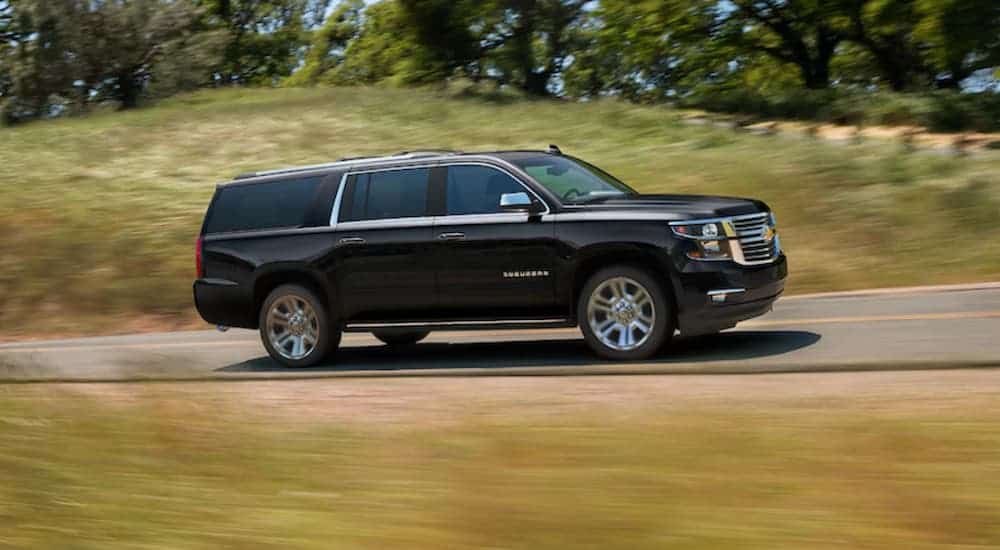 A black 2020 Chevy Suburban is driving on a tree-lined highway. 