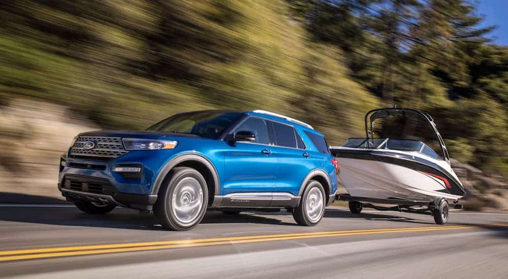 A blue 2020 Ford Explorer, a popular SUV that you will find at King's Ford Automall, is towing a boat. 