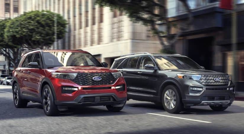 Two 2020 Ford Explorers, red and grey, are stopped at a red light on a busy city street.
