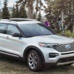 A white 2020 Ford Explorer is parked next to a log cabin in the woods.