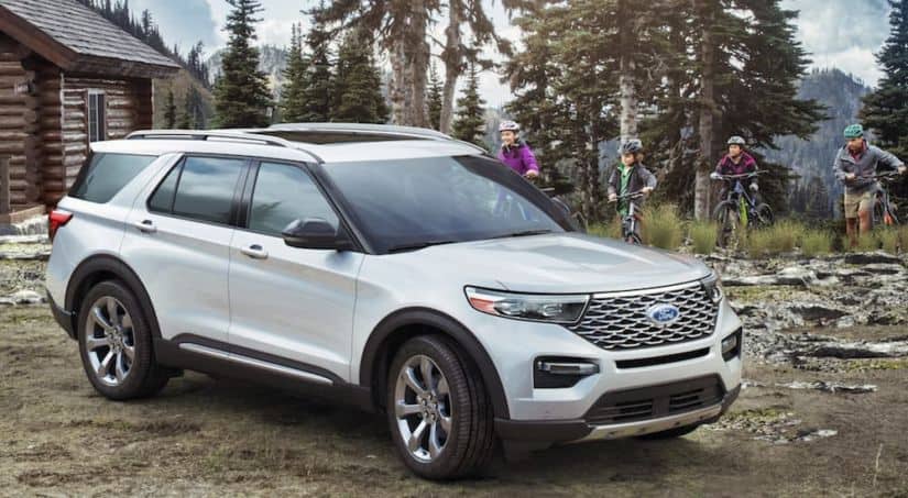 A white 2020 Ford Explorer is parked next to a log cabin in the woods.