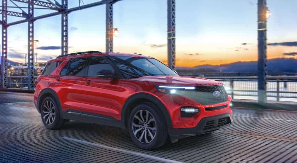 A red 2020 Ford Explorer is driving over a bridge at dusk.