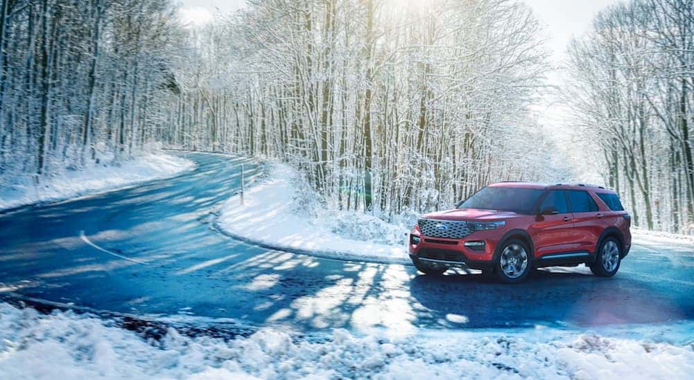 A red 2020 Ford Explorer is driving on a snow road through a wooded area.