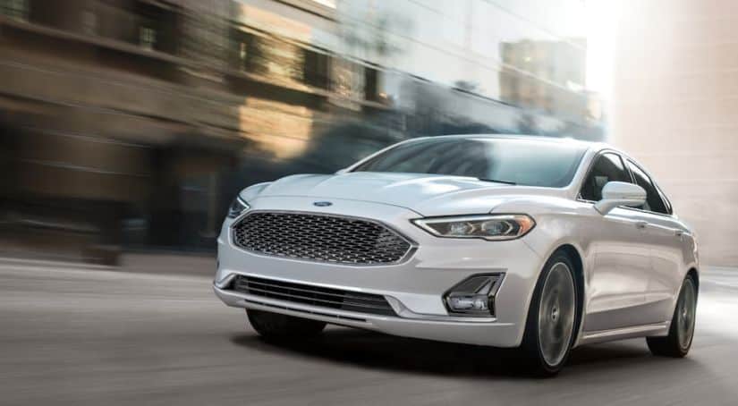 A white 2020 Ford Fusion is driving on a city street.