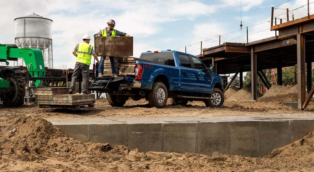 A blue 2020 Ford Super Duty is at a worksite while 2 men load heavy material in the bed. 