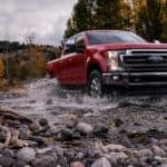 A red 2020 Ford Super Duty is driving through a rocky water way.